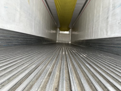 Trailer interior showing ribbed floor and walls, yellow ceiling, open end with light at far end.