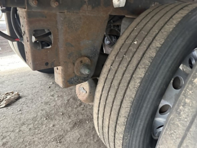 Trailer wheel and undercarriage showing suspension and twin main beam with rust and dirt.