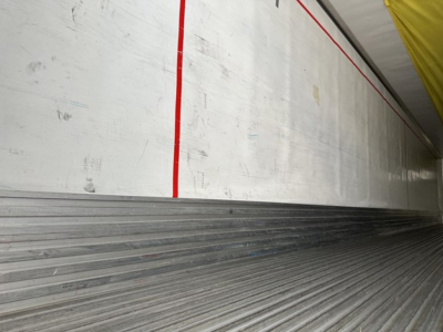 Trailer interior wall with ribbed metal floor and white sidewall showing red vertical stripe.