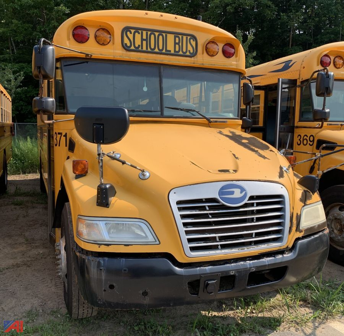 School bus front view with yellow body and black bumper, ‘SCHOOL BUS’ sign on top, blue emblem on grille, and side mirrors.