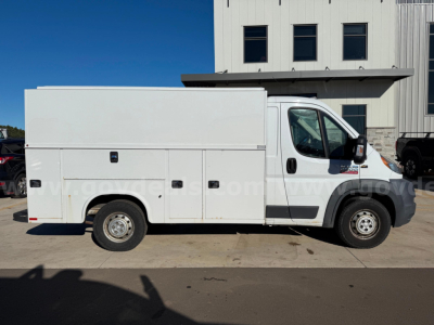 White 2015 Ram ProMaster service utility van profile showing utility storage compartments along side and front door with side mirror.