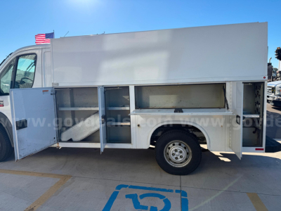 Ram ProMaster service utility van side compartments open showing storage shelves and tool bins in mid section with wheel visible.