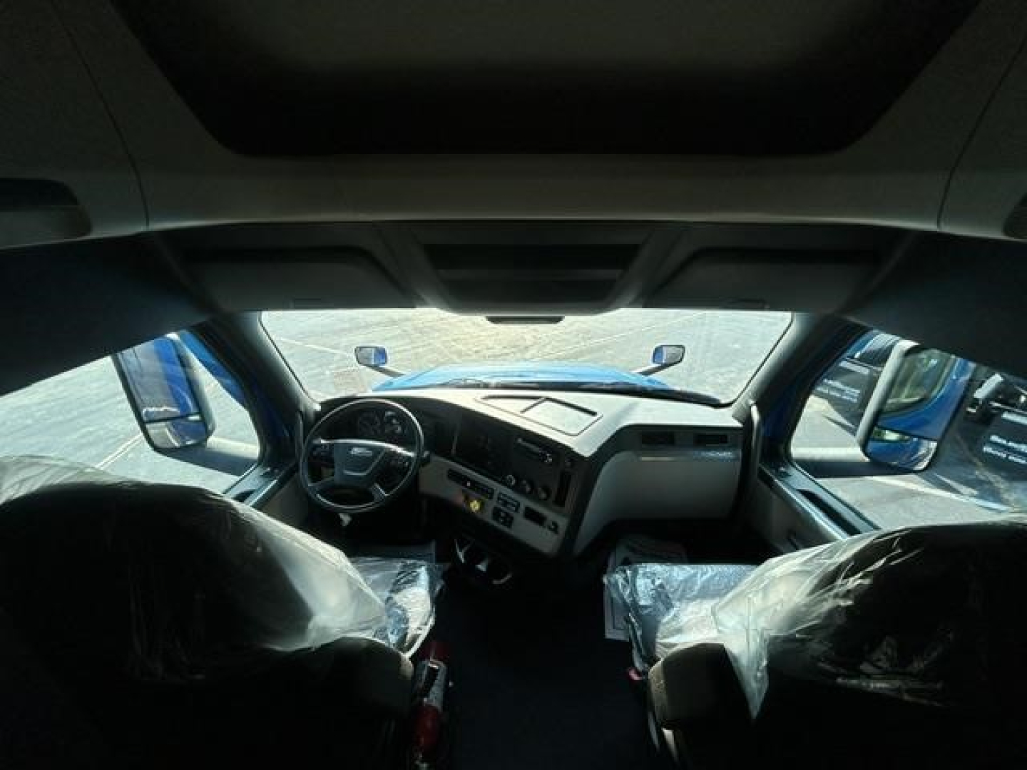 Interior of a Freightliner Cascadia 126 truck cab with plastic-covered seats and dashboard view.