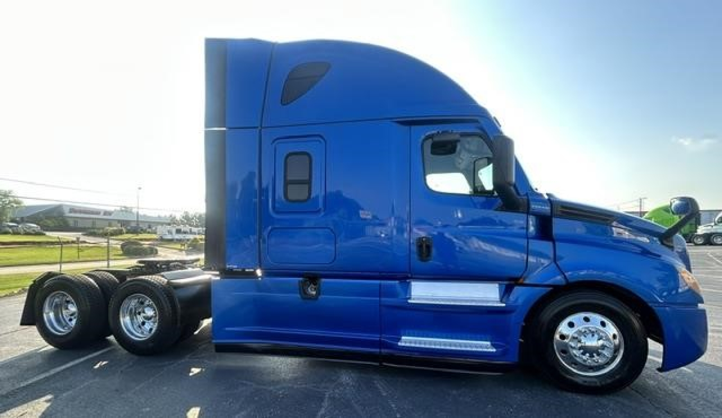 Truck side profile showing a blue Freightliner Cascadia 126 sleeper cab tractor with dual rear axles, chrome wheels, and aerodynamic body lines.