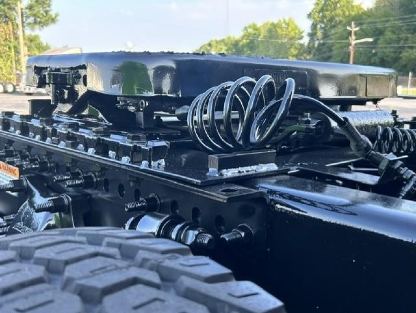 Axle area of a Freightliner Cascadia truck chassis showing coil springs and mounting hardware with a glossy black frame.