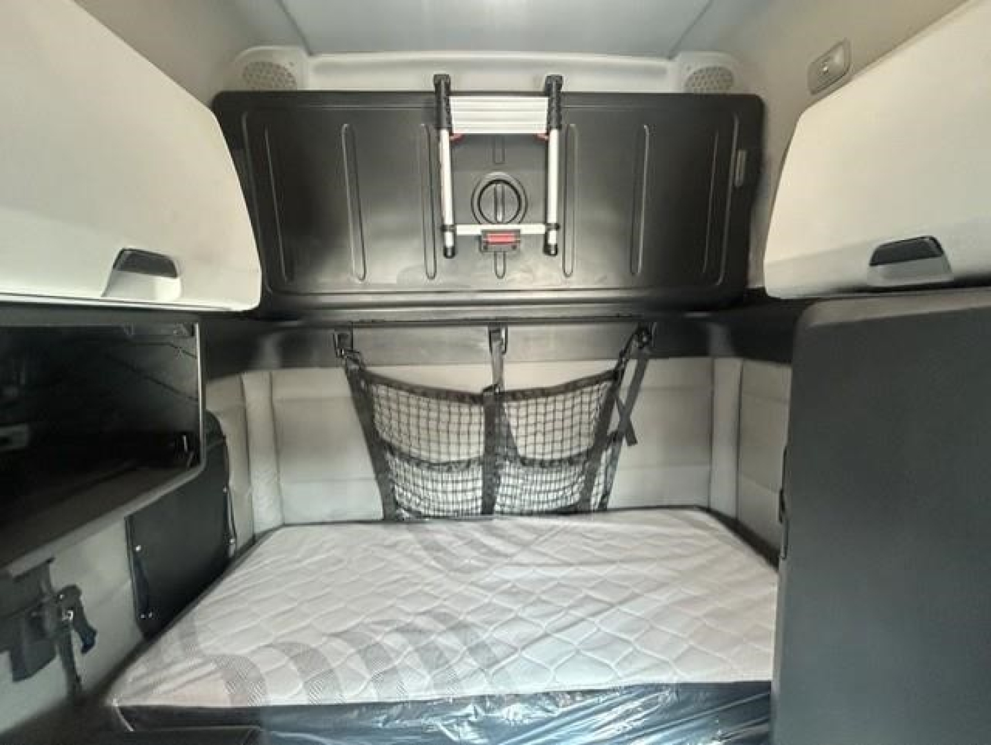 Freightliner Cascadia sleeper cab interior showing bunk bed area with storage nets and shelves.