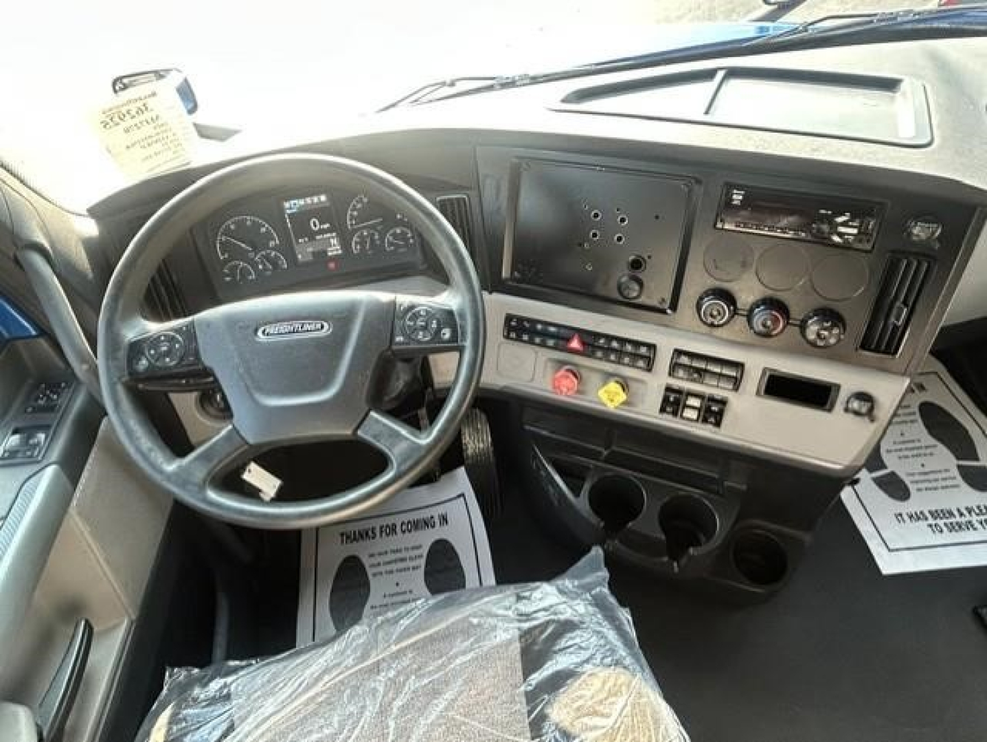 Cab interior of a Freightliner Cascadia showing steering wheel, dashboard, control panel, and gear area.