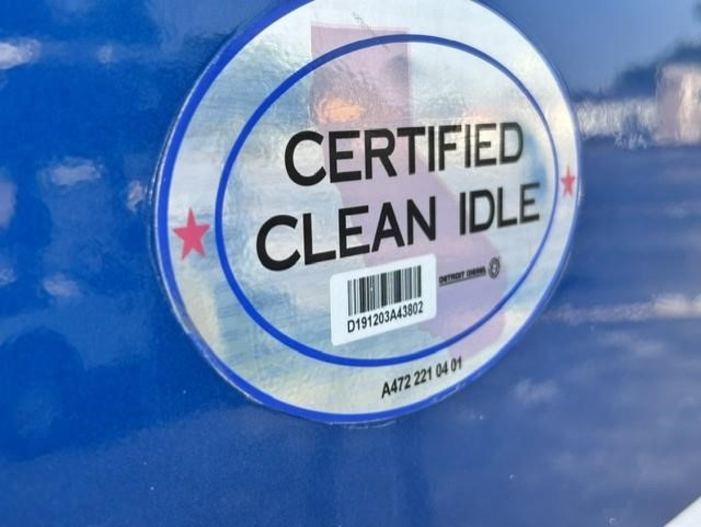 Truck badge showing CERTIFIED CLEAN IDLE sticker with barcode on blue Freightliner Cascadia door.