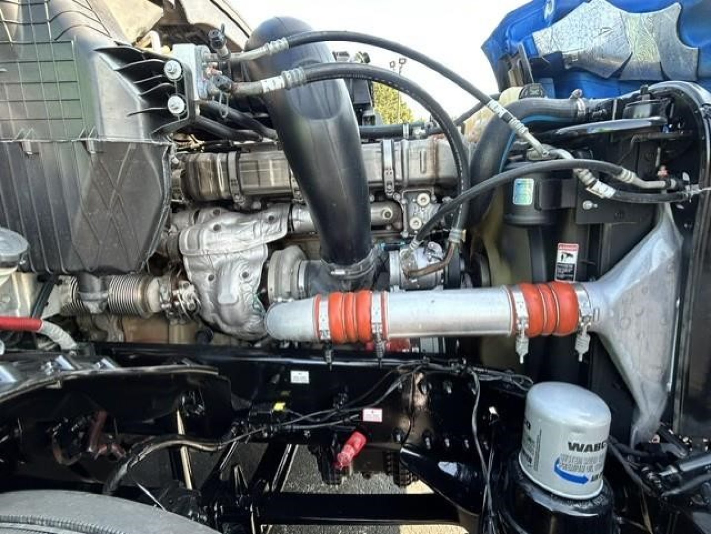 Engine bay of a Freightliner Cascadia showing turbocharger, intercooler piping, coolant hoses, air intake, and WABCO oil filter in serviceable condition.