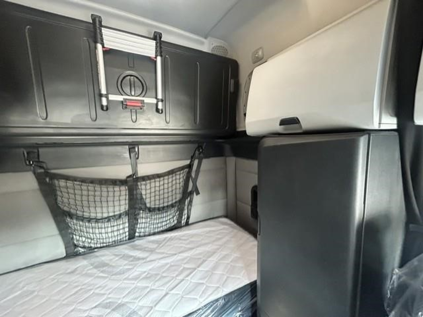 Freightliner Cascadia sleeper cab interior showing cargo nets, storage lockers, and side wall with window shades.