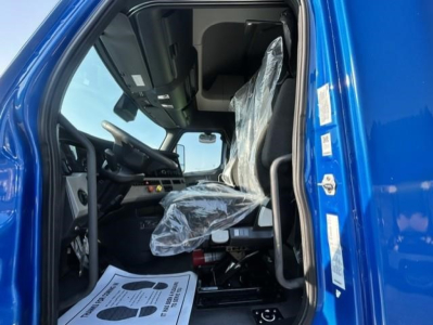 Truck cab interior of a Freightliner Cascadia 126 with blue exterior, plastic-covered driver seat, steering wheel, and dashboard visible.