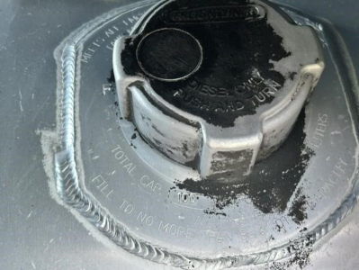 Fuel tank cap and surrounding fuel filler area of a Freightliner Cascadia. Visible are the circular cap with locking ring, fuel filler neck, and embossed text around the cap including ‘FILL TO NO MORE THAN’ and other maintenance marking