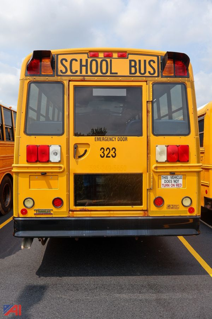 Rear view of a yellow school bus with 'SCHOOL BUS' sign on top, emergency door, and the number 323 visible on the back.