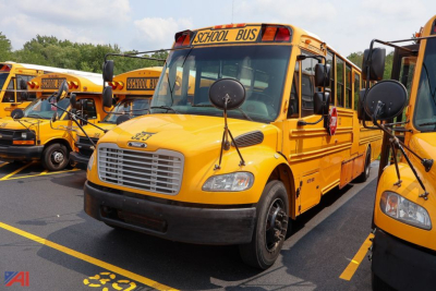 School bus front view showing yellow Freightliner Thomas Saf-T-Liner, with 'SCHOOL BUS' sign on roof and round mirrors.