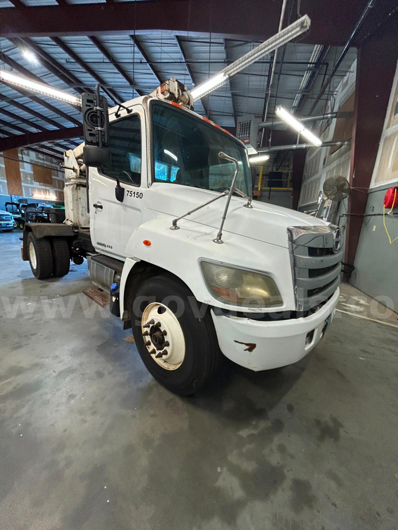 Hino 338 boom truck in a warehouse showing front-left view with crane arm raised.