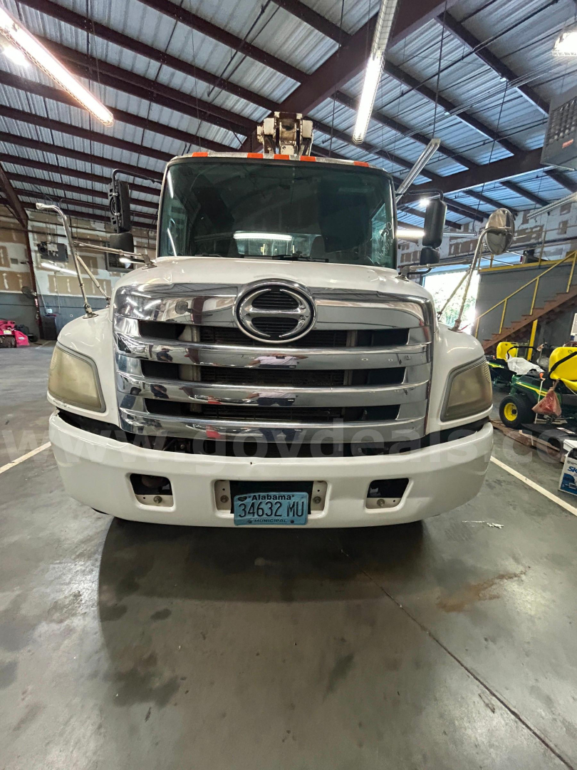Hino 338 boom truck front view showing chrome grille, large bumper, and Alabama license plate in a workshop.