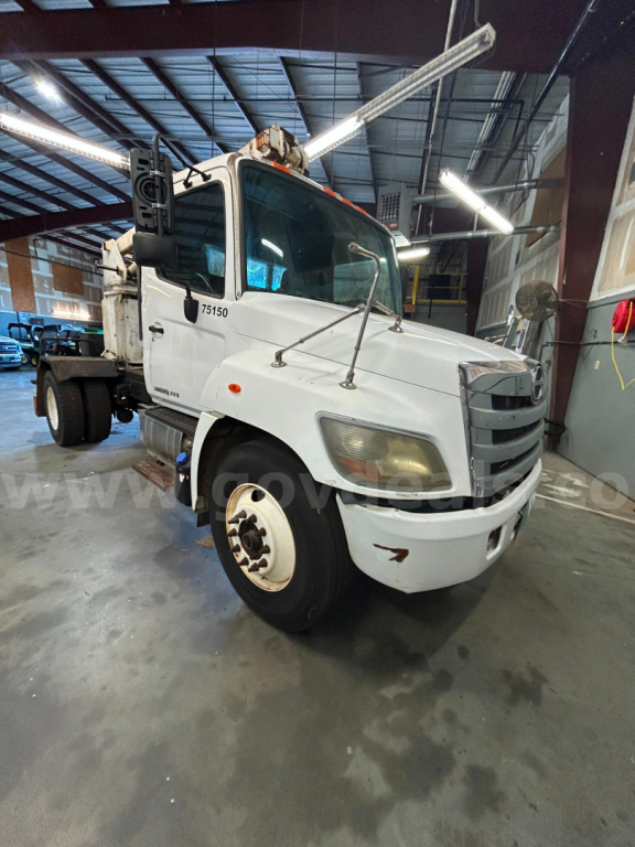 Hino 338 boom truck in a warehouse showing front-left view with crane arm raised.