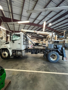 Truck-mounted boom crane on a white 2004 Hino 338 service truck inside a warehouse. Visible text on the cab and crane components includes HINO logo and model numbers on doors and equipment.