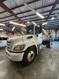 2004 Hino 338 boom truck in a warehouse showing front and side views with crane on bed and white cab.