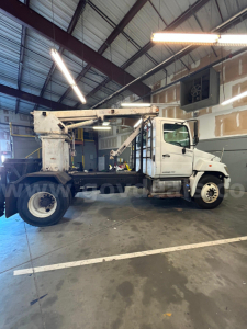 Truck mounted boom crane in a workshop showing rear long arm and white cab with boom structure.