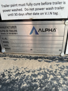 Trailer manufacturer plate showing Alpha Trailers logo with VIN, model ASB1, date, weight and other specs. Upper text mentions wash instructions for trailer.