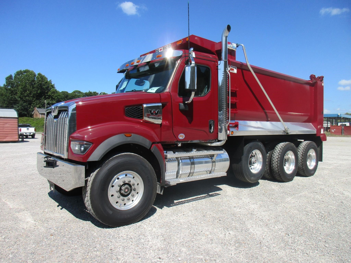 Dump truck in serviceable condition showing red Western Star 49X dump bed and chrome fuel tanks; three axles, heavy-duty tires, side mirrors, and cab with roof lights.