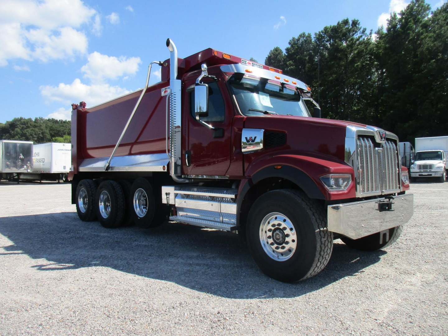 Western Star 49X dump truck in maroon showing cab and aluminum dump body with chrome front grille and dual rear axles; sunlight and gravel lot.