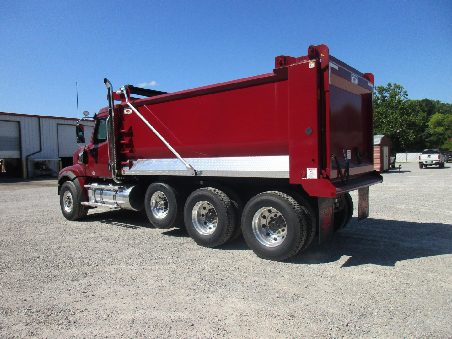 Red Western Star 49X dump truck in a gravel lot, side view showing the dump bed doors and wheels.