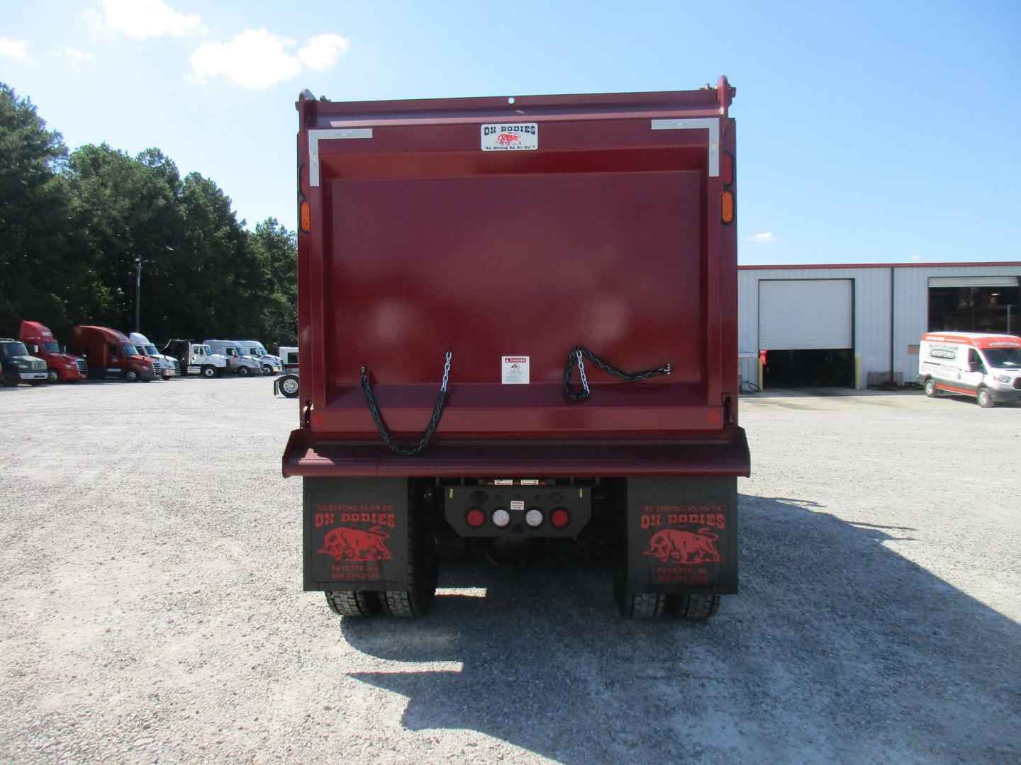 Dump truck bed rear view showing rear bumper with hydraulic hoses and lights.