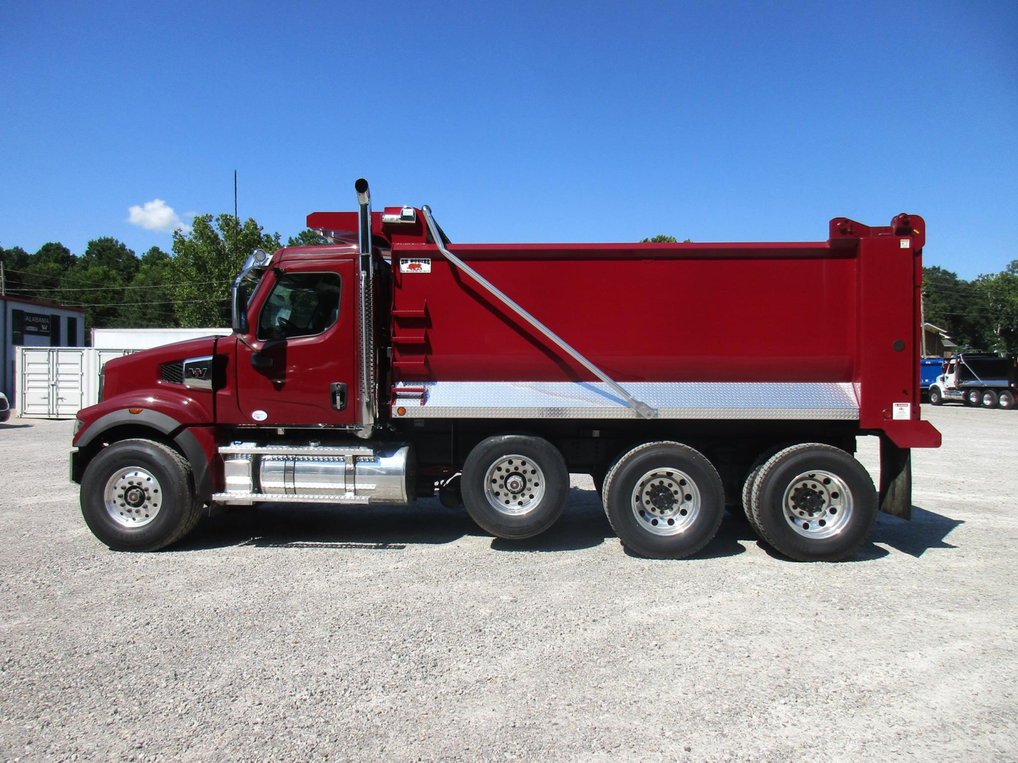 Truck side view showing a red Western Star 49X dump body with three rear axles and chrome fuel tanks.