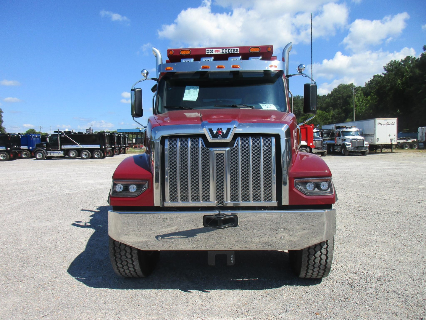 Front view of a red 2027 Western Star 49X dump truck with chrome grille, large bumper, and dual mirrors.
