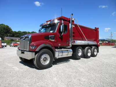 Dump truck showing red Western Star 49X with chrome grille and dump bed, three rear axles, and fuel tanks on side.