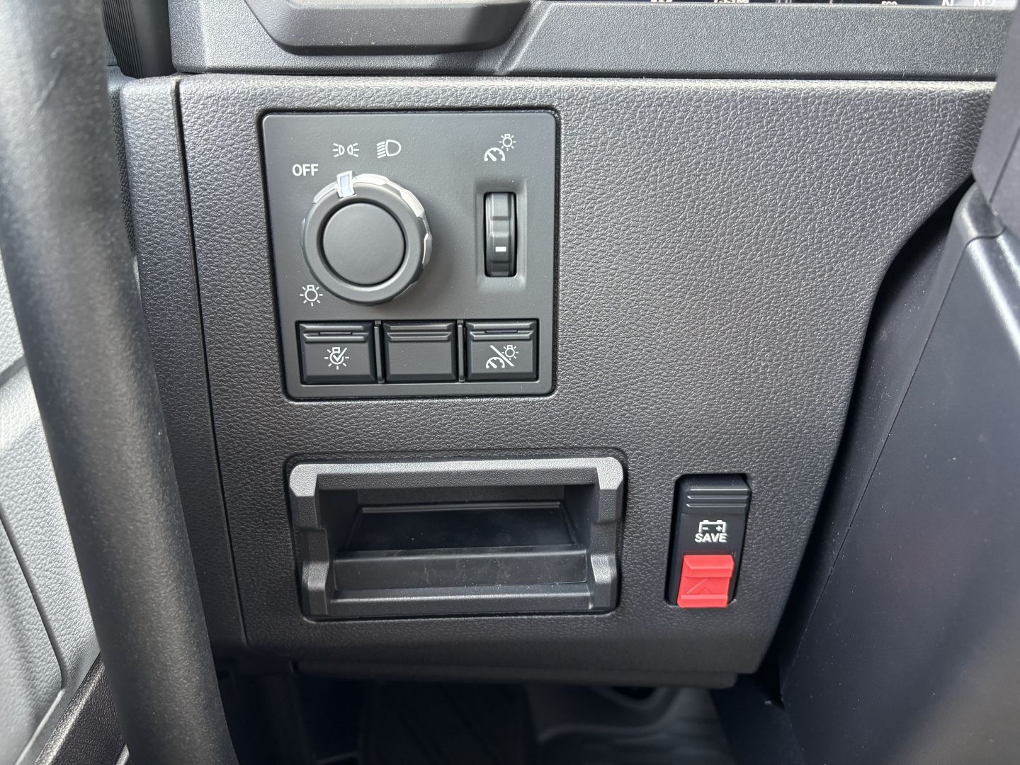 Dashboard controls showing headlight switch with dial, 4 auxiliary buttons, a small cubby hole, and a red SAVE button on the right.