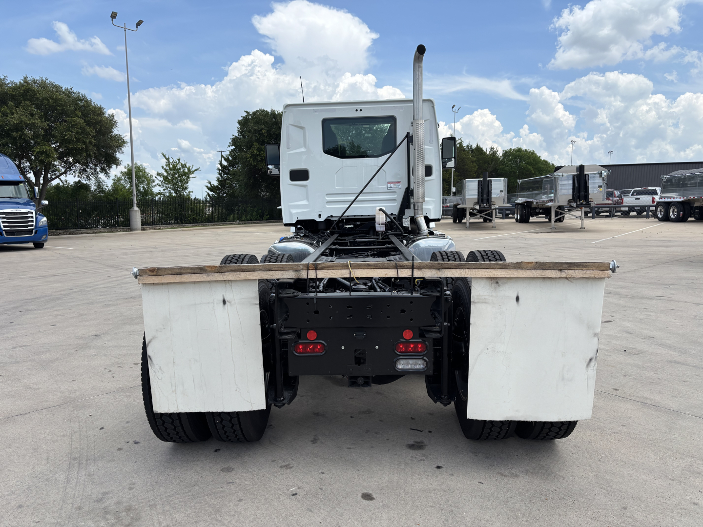 Truck rear view showing Mack AN64 chassis with dual rear wheels and hitch, cab in background, white mud flaps, flatbed rail at rear.