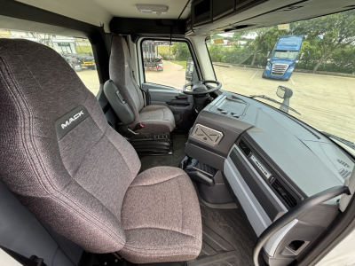 Cab interior of a 2027 Mack AN64 dump truck showing driver seat, passenger seat, steering wheel, dashboard, and large windshield.