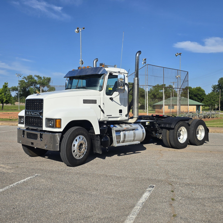 Mack PI64T conventional daycab truck in a parking lot, side view showing dual rear axles, cab-mounted exhaust, chrome fuel tanks, and front grille with Mack emblem.
