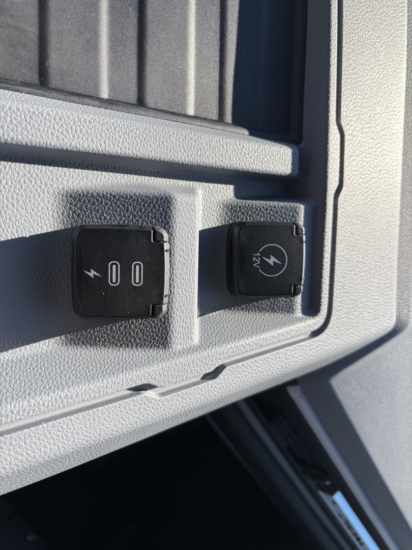 Truck interior switch panel with 12V power outlet and auxiliary power symbol, plus a 24V DC socket cap visible.