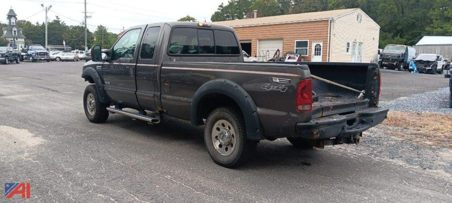 2007 Ford F-250 Super Duty pickup truck with extended cab and single rear wheel, black/gray, viewed from rear left in a lot with tailgate down.