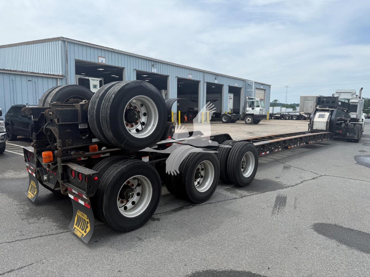 Beams trailer in a yard showing long flatbed with multiple axles and spare tires.