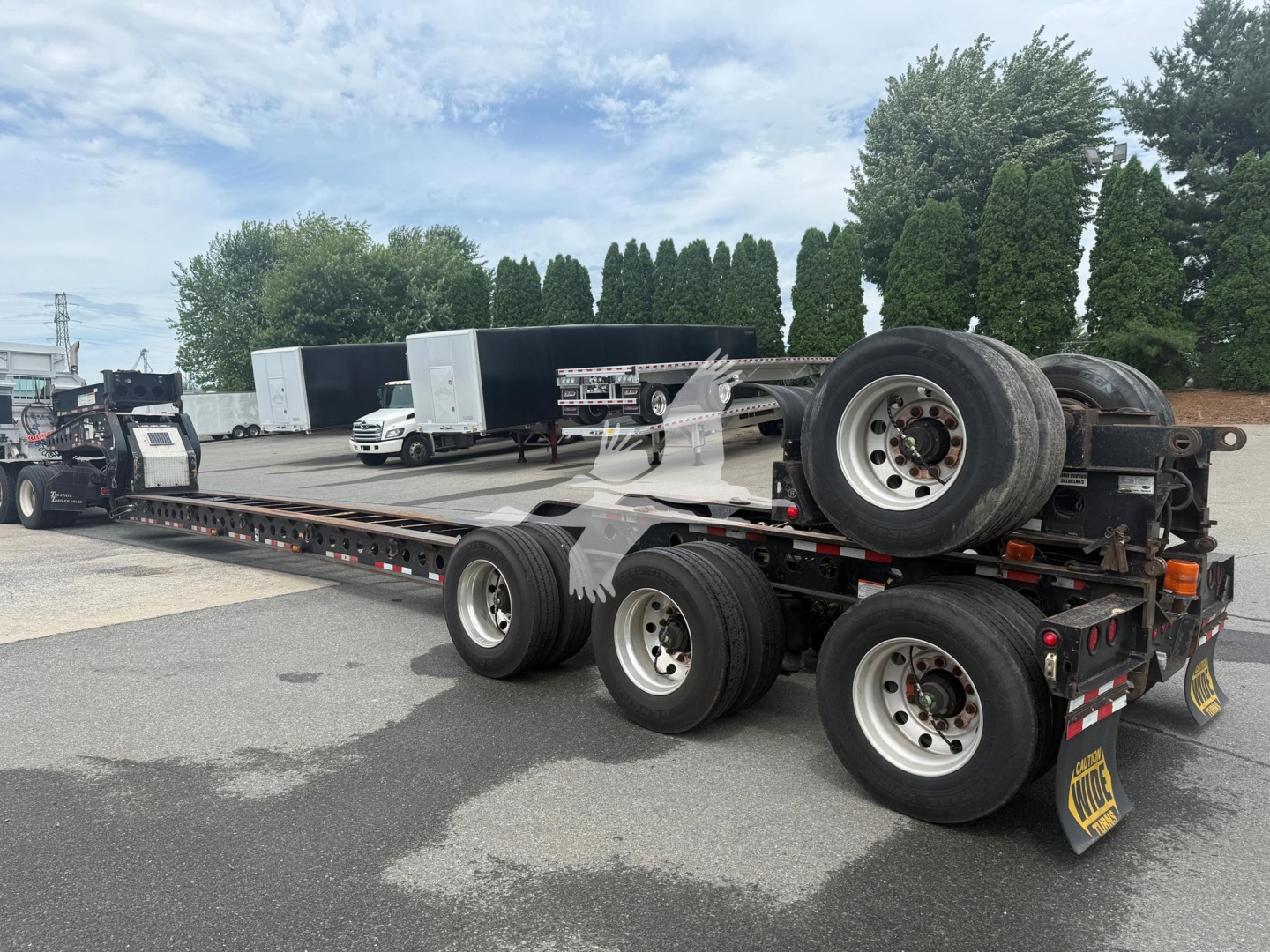 2014 Etnyre beam lowboy trailer shown in a parking lot with dual rear axles, spare wheel on the gooseneck, and wheel chocks; no legible serials or model text visible on image.