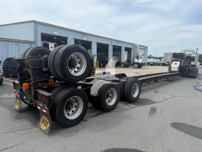 Beams trailer in a yard showing long flatbed with multiple axles and spare tires.