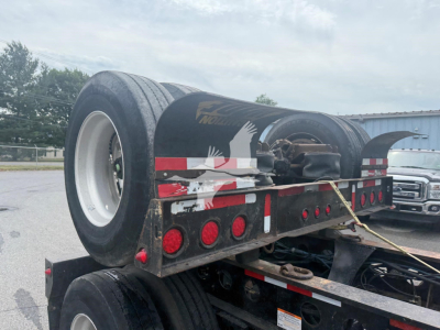 Lowboy trailer rear view showing dual rear tires, black metal frame, red circular lights, and reflective tape; 2014 Etnyre beam trailer branding on fender and wheel; VIN plate not visible.