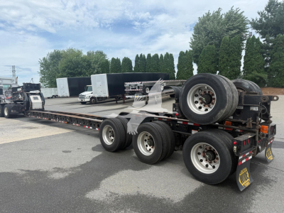 2014 Etnyre beam lowboy trailer shown in a parking lot with dual rear axles, spare wheel on the gooseneck, and wheel chocks; no legible serials or model text visible on image.