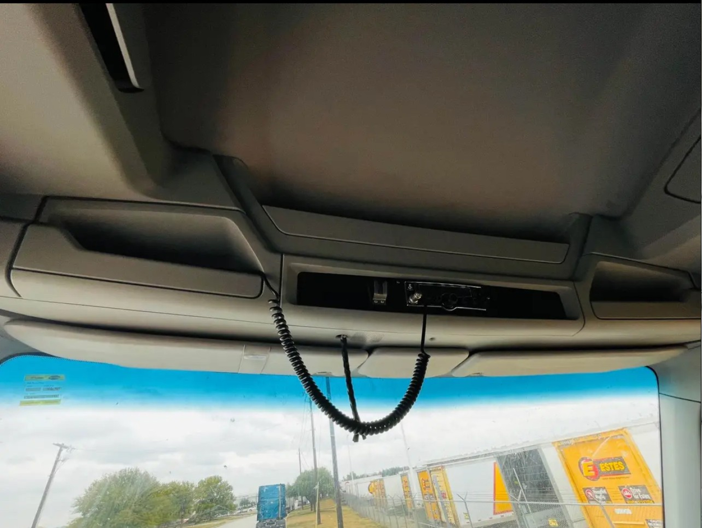 Cab interior overhead area of a Kenworth T680 showing a coiled cord hanging from the overhead console and sun visors. No other readable text visible.