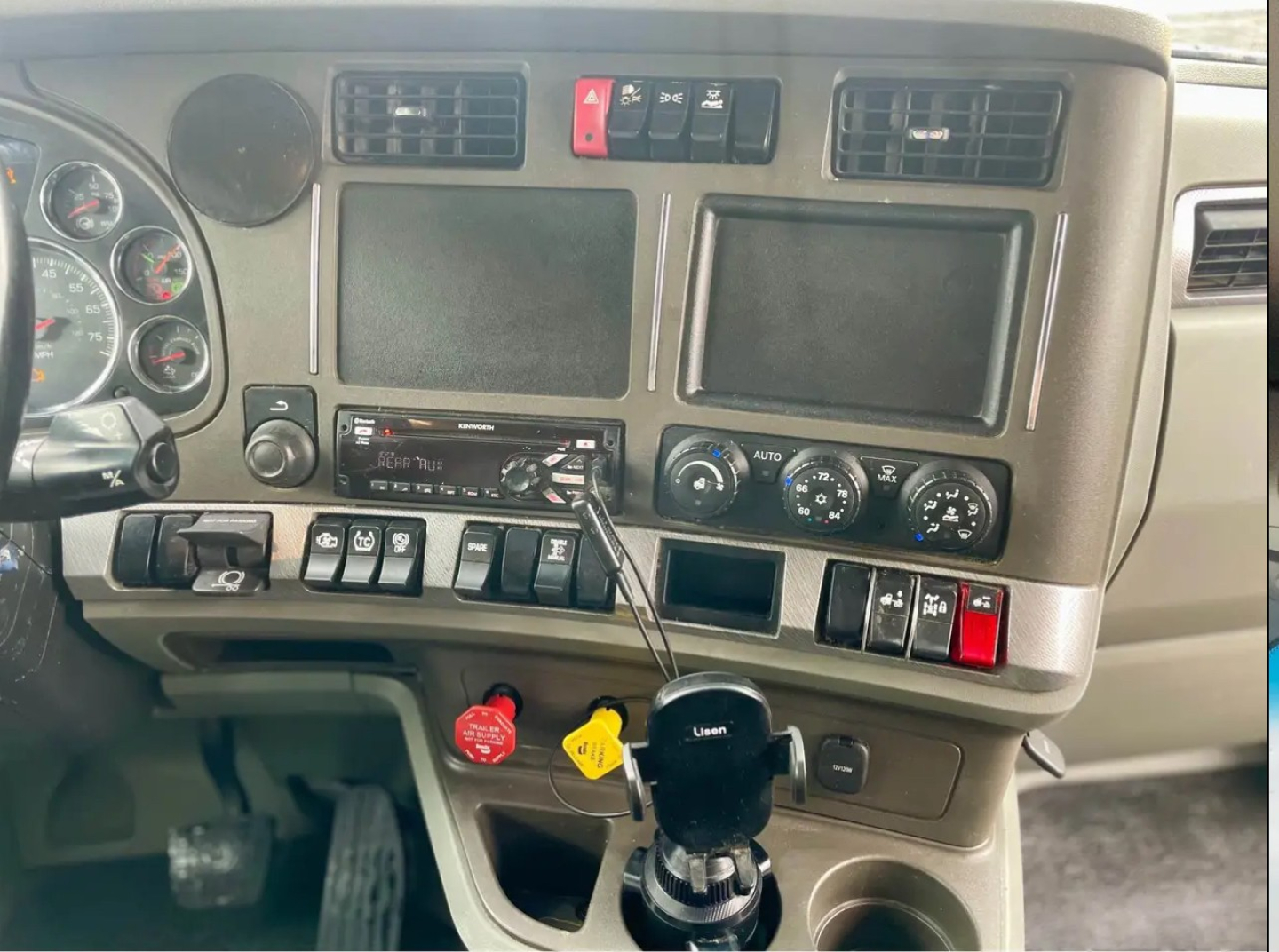 Kenworth T680 dashboard showing dual large display screens, climate controls, ignition with red and yellow switches, and gear shifter with key fob inserted.