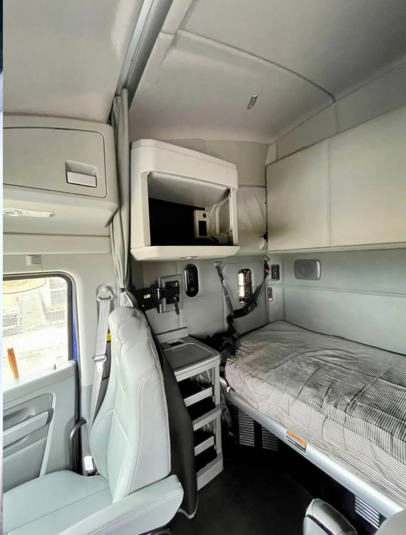 Kenworth T680 sleeper cab interior showing bunkbed area with storage cabinet, overhead console, and driver's seat.