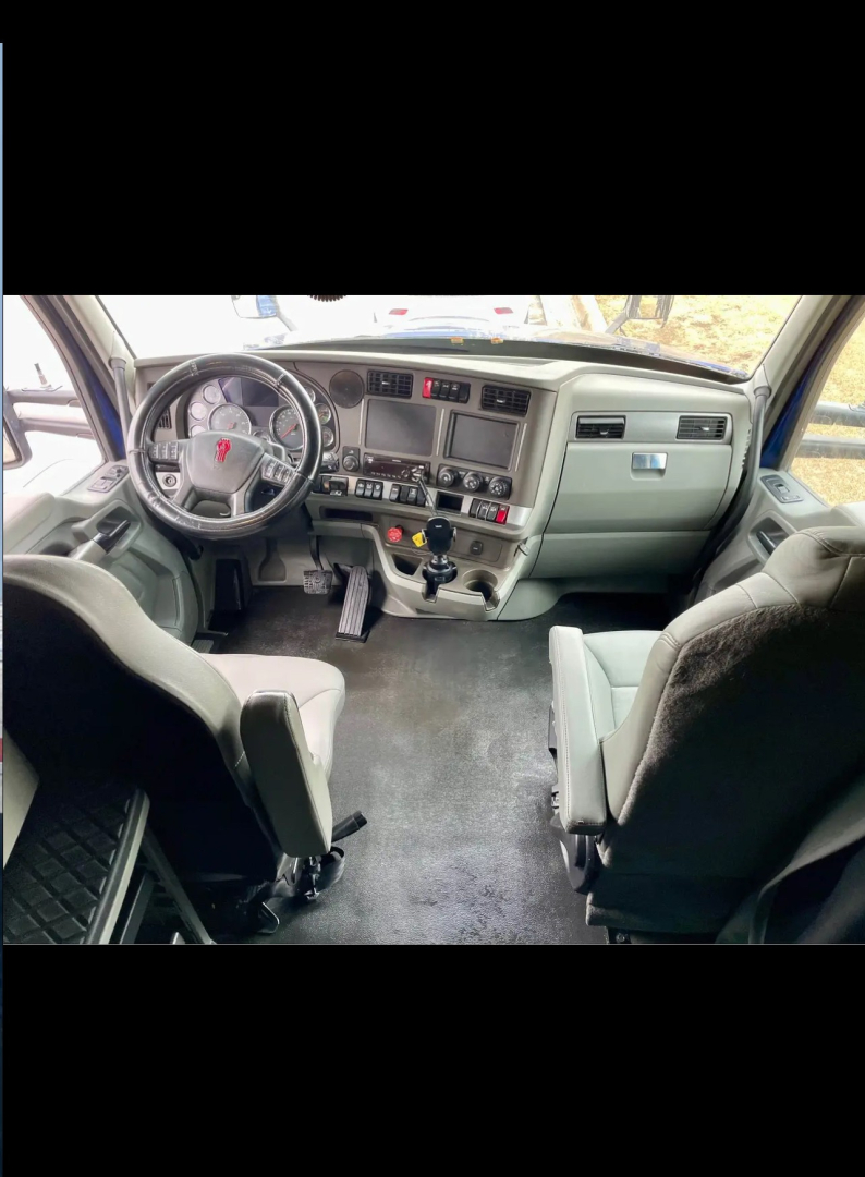 Truck interior showing steering wheel, dashboard, gear shifter, and front seats in a Kenworth cab.
