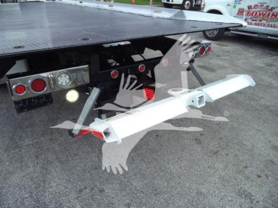 Rear underside view of a rollback tow truck showing a silver multi-hook hitch and platform with taillights and hydraulic components.