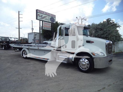 Peterbilt 337 rollback truck in serviceable condition, side view showing tow bed and cab, in a dealership lot.