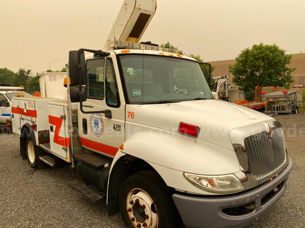 International 4300 bucket truck with a boom lift, white with orange stripe, showing side text and numbers on cab and body.